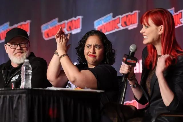 Red-haired panel moderator (Janet Varney per the press release) holding a mic beside clapping panelists at the NYCC 2026 Avatar panel