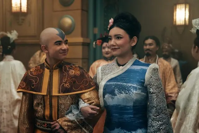 Season 2 still: Aang and Katara in formal Earth Kingdom attire walking arm in arm at an elegant gathering