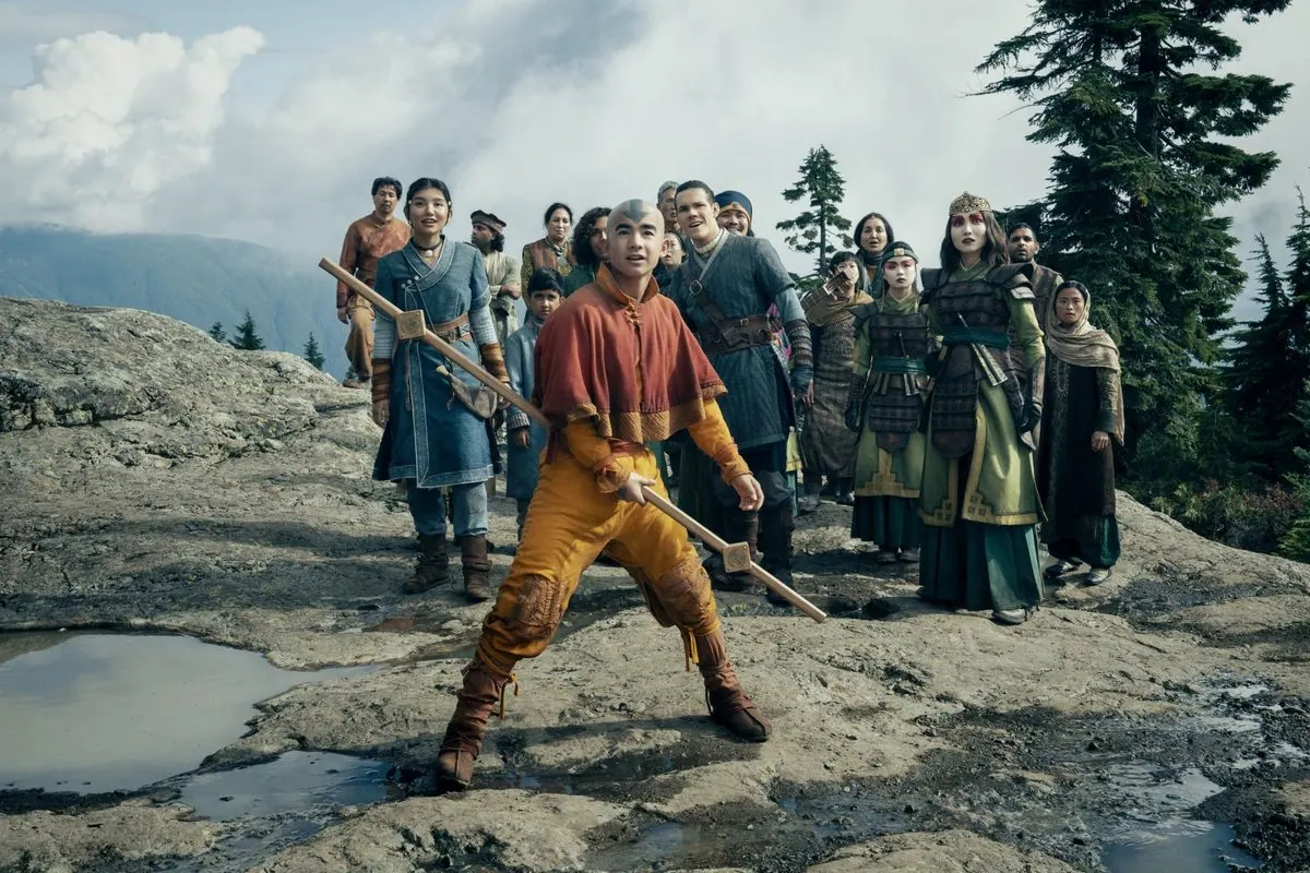 Season 2 first-look still: Aang with his staff leading Katara, Sokka, Suki and a crowd across a rocky mountain ledge