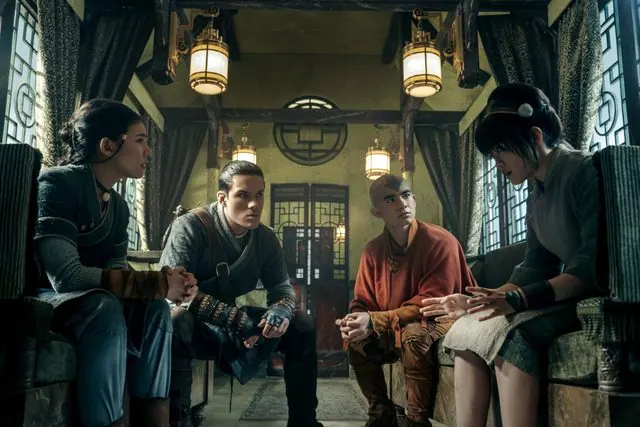 Season 2 first-look still: Katara, Sokka, Aang and Toph seated together in an ornate lantern-lit room