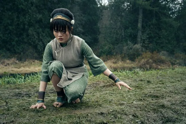 Season 2 first-look still: Miya Cech as Toph crouching barefoot in a forest clearing, hand on the ground