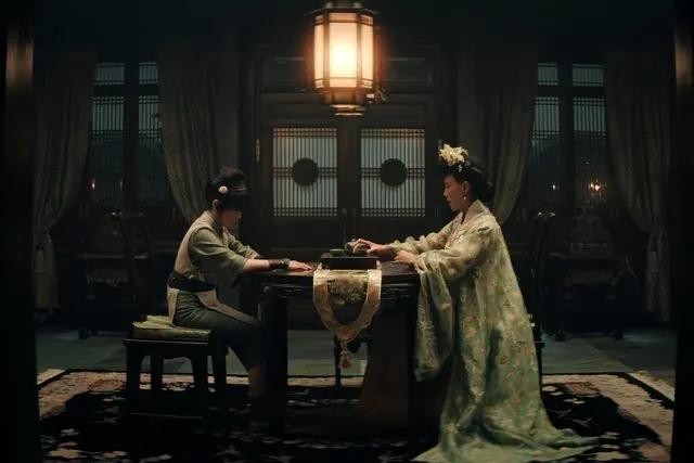 Season 2 still: Toph and Crystal Yu as Lady Beifong seated across an ornate table