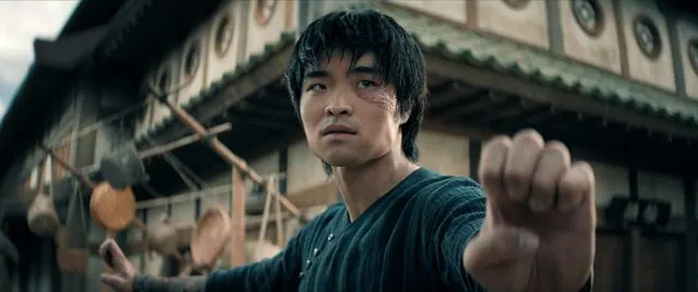 Season 2 Episode 2 still: Dallas Liu as Zuko throwing a punch in an Earth Kingdom street