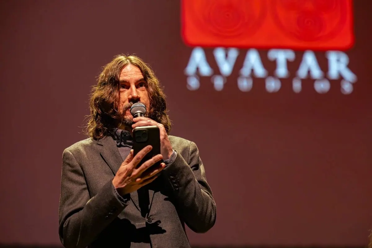 Speaker with long hair addressing a concert audience in front of the projected Avatar Studios logo; the official tour site names the file as Bryan Konietzko