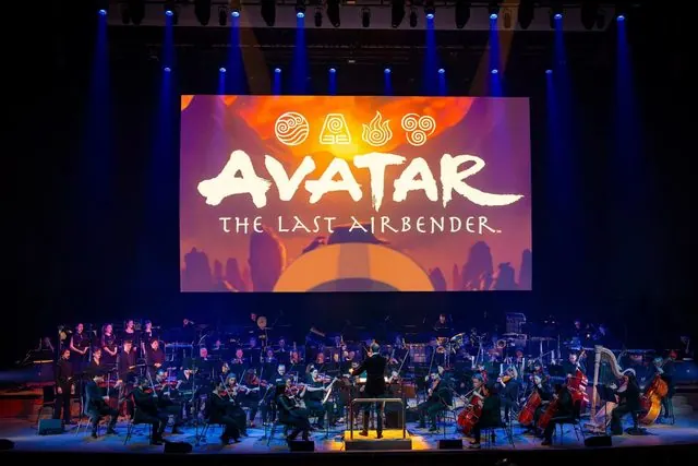 Orchestra performing beneath the Avatar: The Last Airbender title card on the big screen, blue stage lighting