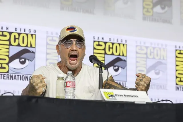 Dave Bautista roaring with fists up at the Avatar Aang Hall H panel, name card visible, SDCC 2026